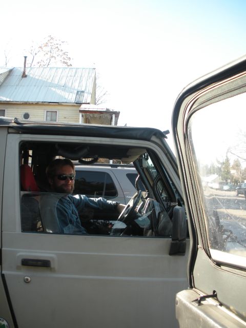 1971 Ford Bronco - Man sits in the driver's seat of a silver SUV, with another vehicle behind.