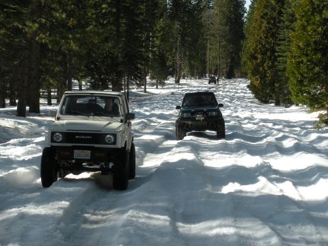 1971 Ford Bronco - Suzuki Samurai SUVs navigate a snowy path in a wooded area.