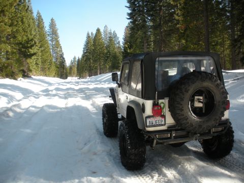 1971 Ford Bronco - A white Jeep Wrangler navigates a snow-covered road through a forest.