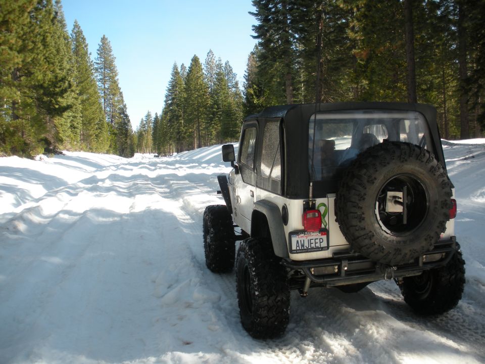 White Jeep Wrangler with soft top and spare tire on snowy road