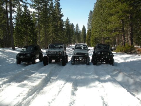 1971 Ford Bronco - Four off-road vehicles are parked in a snowy forest, likely on a trail.