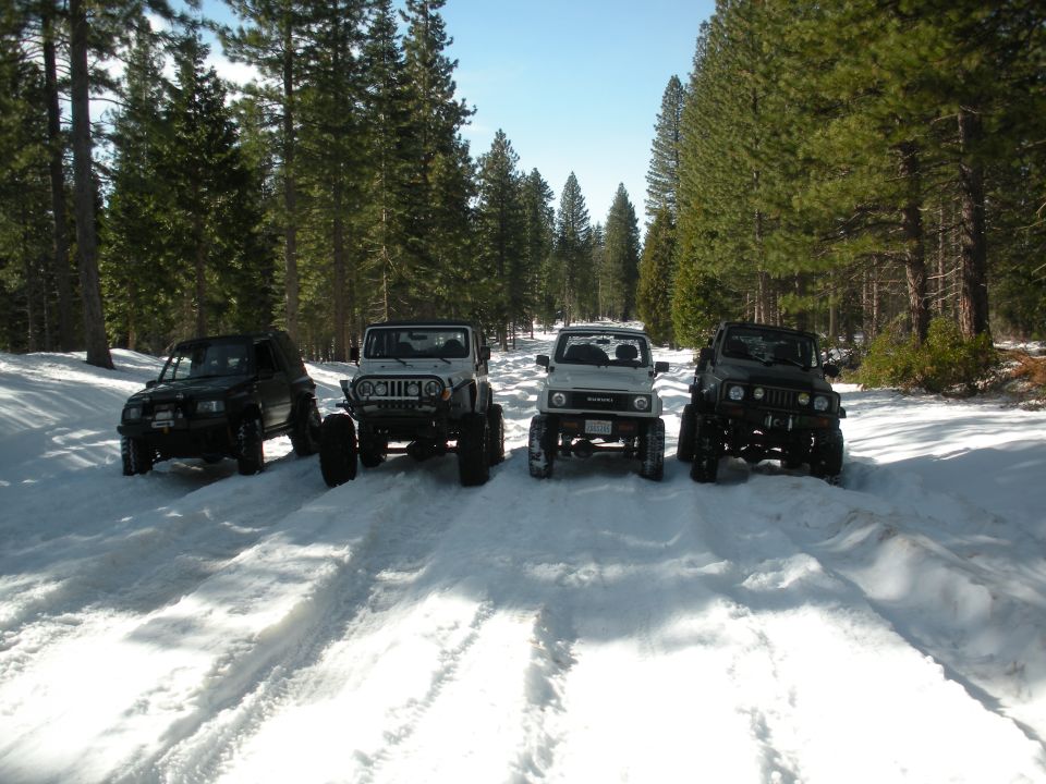 Four modified off-road vehicles parked in a snowy forest road