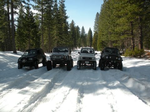 1971 Ford Bronco - Several off-road vehicles are lined up on a snow-covered path in a forest.