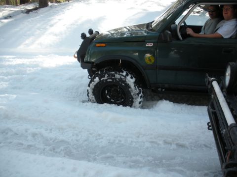 1971 Ford Bronco - A green SUV navigates a snowy terrain, its front tire deep in the snow.