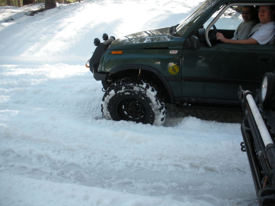 Green SUV with off-road tires stuck in snow, front wheel visible