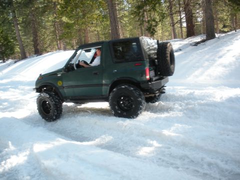 1971 Ford Bronco - SUV navigates a snowy forest road, kicking up snow with its tires.