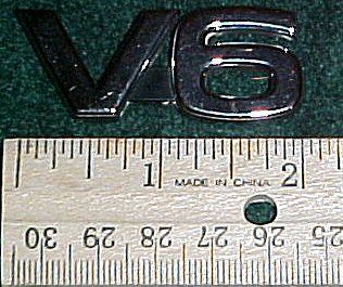 2003 Ford Expedition - Close-up of a V6 engine badge next to a ruler, indicating its size.