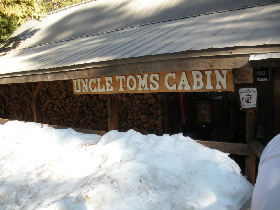 Uncle Toms Cabin sign above stacked firewood and snow