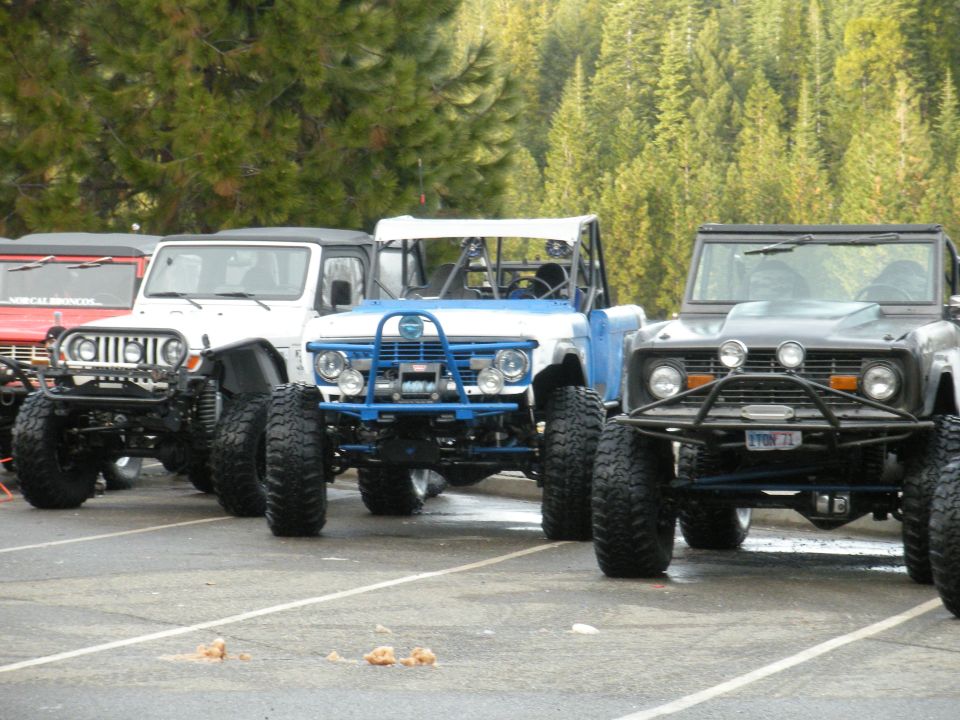 1971 Ford Bronco and other modified SUVs parked in a lot with trees in background. License plate reads 'LYON 71'