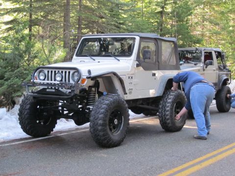 1971 Ford Bronco - A white Jeep Wrangler is being worked on by a person, with another vehicle behind it on a road.