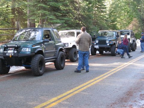 1971 Ford Bronco - Several off-road vehicles are parked on a paved road surrounded by trees.