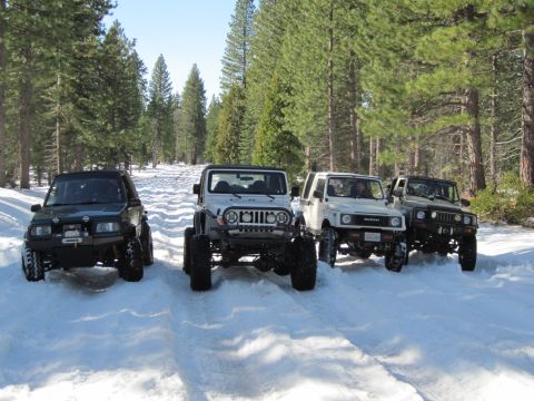 1971 Ford Bronco - A convoy of four-wheel-drive vehicles navigates a snow-covered path surrounded by tall pine trees.
