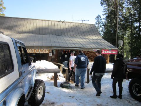 1971 Ford Bronco - A light blue SUV with a white top is parked in the snow outside a cabin, with several people entering the building.