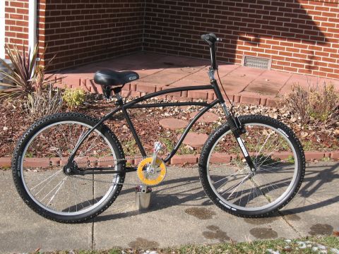 1994 Ford Bronco - A black bicycle with a distinctive yellow chainring and knobby tires is shown from the side, resting on a concrete sidewalk.
