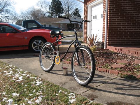 1994 Ford Bronco - A custom bicycle sits on a driveway next to a red car and a brick house.