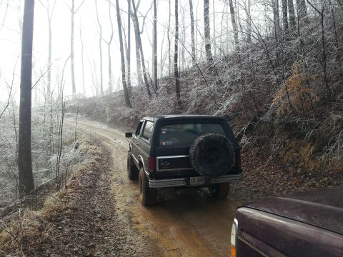 1986 Ford Bronco - A black Ford Bronco navigates a muddy, wooded path in foggy conditions.