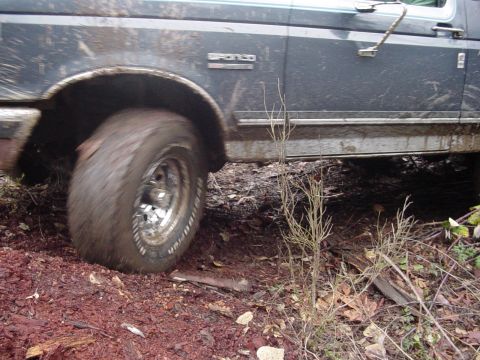 1987 Ford Bronco - A Ford Bronco navigates a muddy, off-road trail, with its tire kicking up dirt.