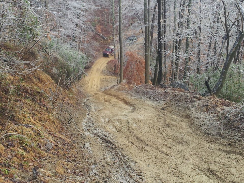 Off-road vehicle climbing a steep, muddy hill in a wooded area with icy trees