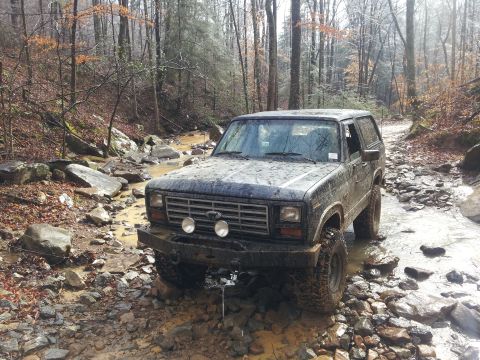 1986 Ford Bronco - This Ford Bronco navigates a challenging off-road trail with water and rocks.