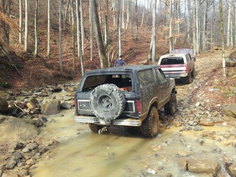 1986 Ford Bronco - A black 1986 Ford Bronco navigates a rocky, muddy trail with another SUV following behind.
