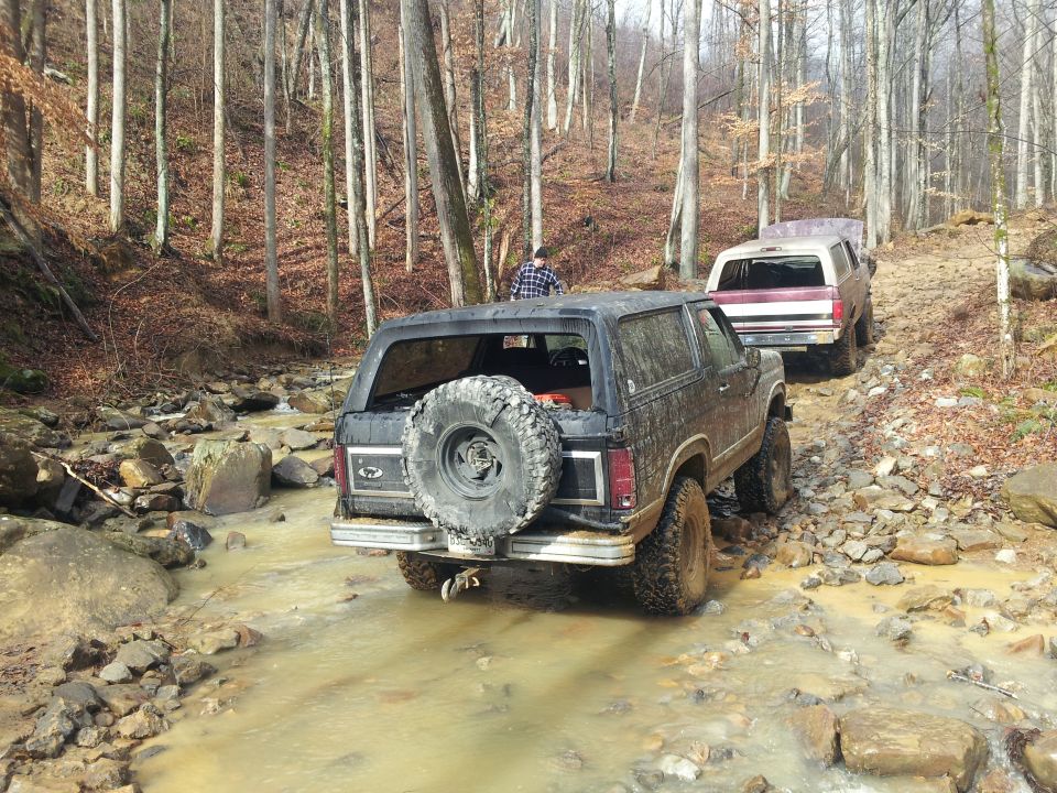 Black 1986 Ford Bronco rear view, driving off-road through mud and rocks