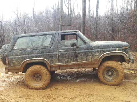 1986 Ford Bronco - This off-road vehicle is covered in mud after driving through a wet, wooded area.