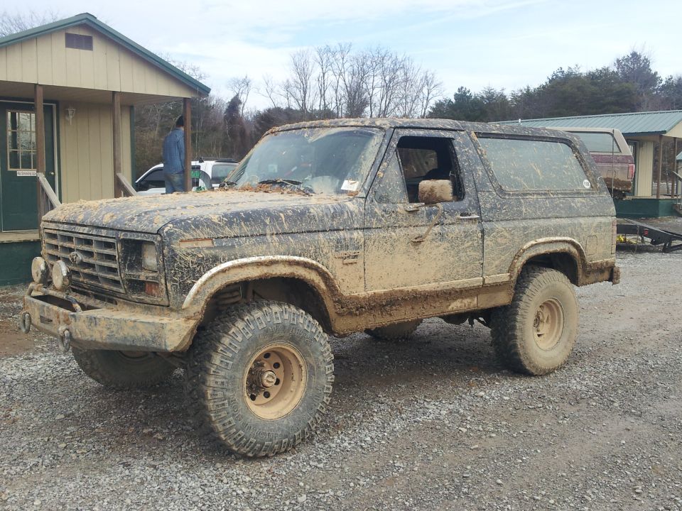Mud-covered 1980s Ford Bronco, 3/4 front view, with off-road tires and auxiliary lights