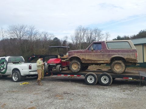 1986 Ford Bronco - A maroon 1986 Ford Bronco is loaded onto a trailer behind a white pickup truck.