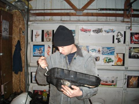 1989 Ford Probe - Man applies sealant to an oil pan in a garage decorated with vintage car photos.