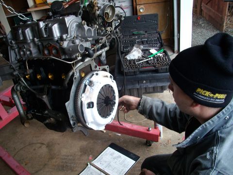 1989 Ford Probe - Mechanic works on an engine assembly with a toolbox and manual open.