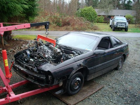 1989 Ford Probe - A black coupe has its engine removed and is supported by a red engine hoist.