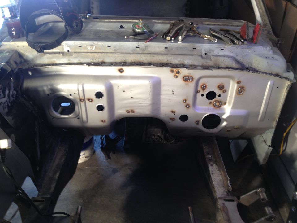 Bare metal vehicle firewall on frame during restoration with rust and holes