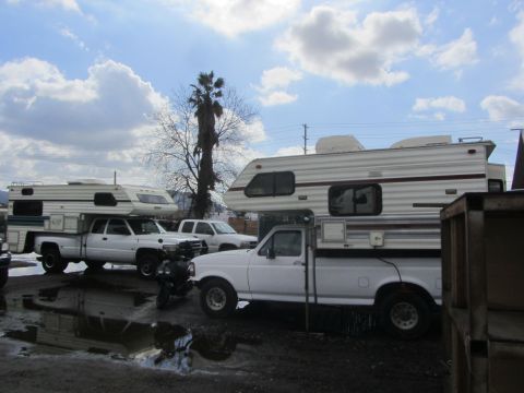 1986 Yugo GV - Several pickup trucks are parked with camper shells, under a cloudy sky.