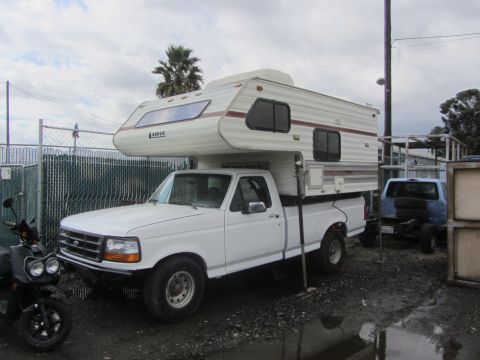 1986 Yugo GV - A white Ford F-Series truck is equipped with a white Lance camper shell and parked next to a blue truck.