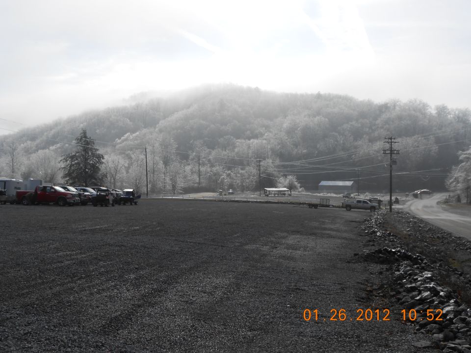 Several trucks and trailers parked in a gravel lot with a frosted hillside in the background