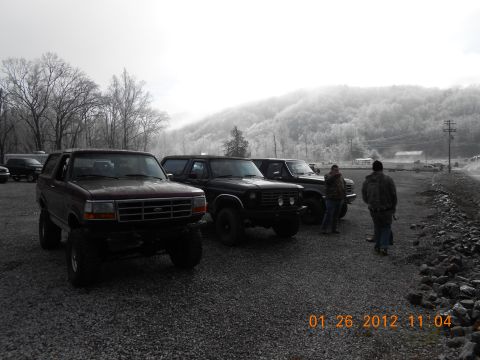 1986 Ford Bronco - A group of SUVs, including a Ford Bronco, are parked outdoors on a cloudy day with a mountain range in the distance.