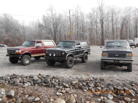 1986 Ford Bronco - Three Ford Broncos parked on a gravel lot with trees in the background.