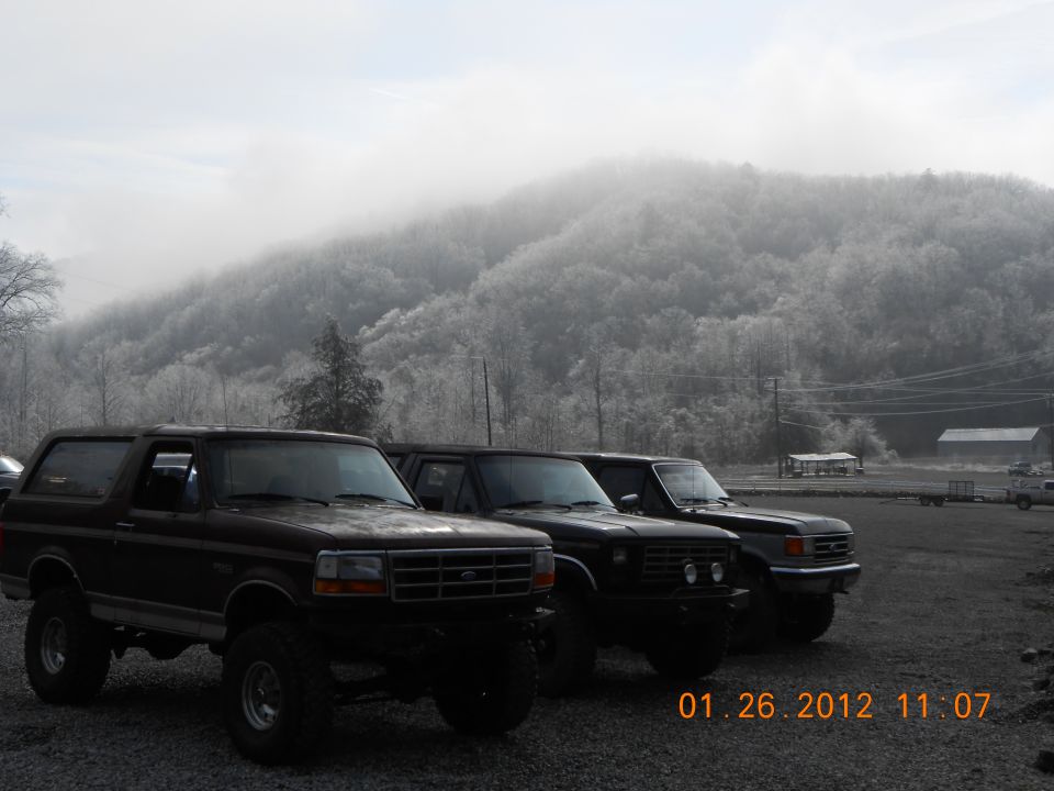 Three black Ford Broncos parked in a lot with a misty mountain in the background