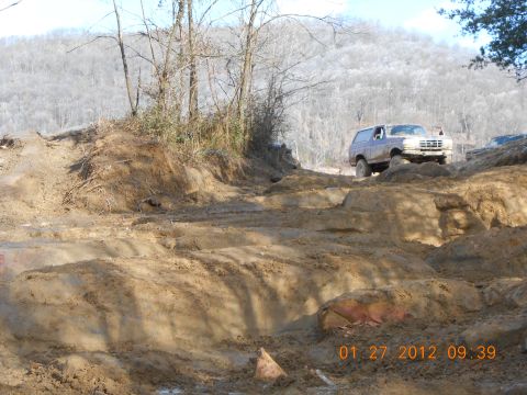 1986 Ford Bronco - A 1986 Ford Bronco navigates a challenging, muddy off-road course on a clear day.