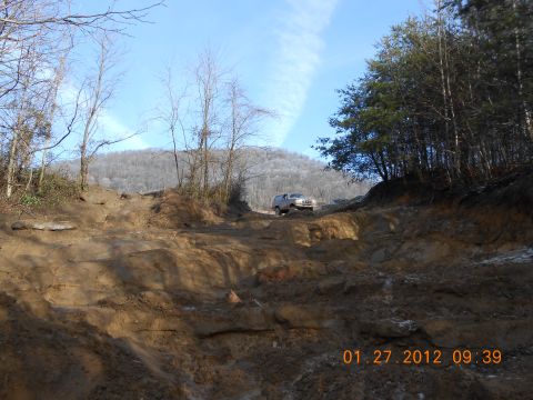 1986 Ford Bronco - A silver SUV navigates a challenging muddy terrain under a clear blue sky.