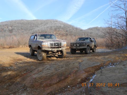 1986 Ford Bronco - Two off-road Broncos are seen on a dirt path under a clear sky.