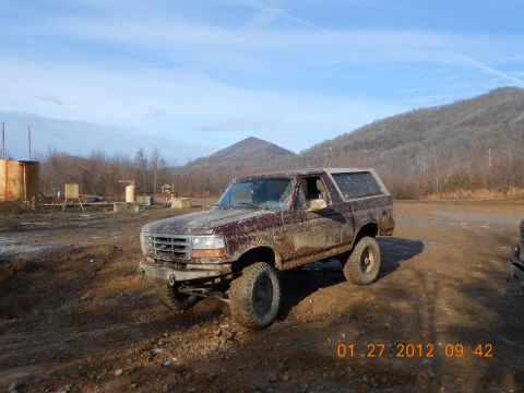 1986 Ford Bronco - Ford Bronco parked on a muddy road with industrial equipment in the background.