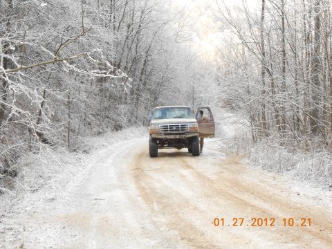 1986 Ford Bronco - A brown Ford F-Series truck is parked on a snowy dirt road with trees covered in ice and snow.