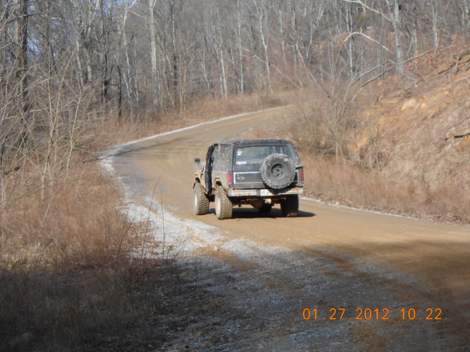1986 Ford Bronco on a winding dirt road, spare tire mounted on rear door