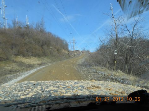 1986 Ford Bronco - A dirt road winds uphill through a wooded area with power lines overhead, seen from the perspective of a vehicle's dashboard.