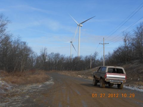 1986 Ford Bronco - A Ford Bronco drives down a dirt road near wind turbines.