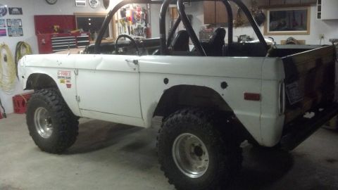 1970 Ford Bronco - A white Ford Bronco with a roll cage and large tires sits in a garage, appearing to be undergoing some work.