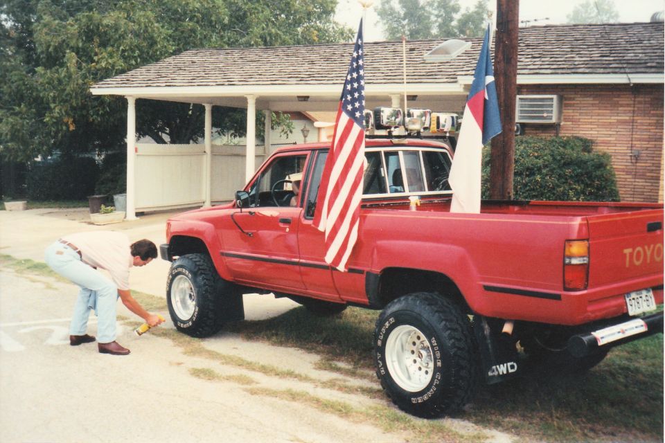 Red Toyota pickup truck with American and Christian flags, lifted with large tires