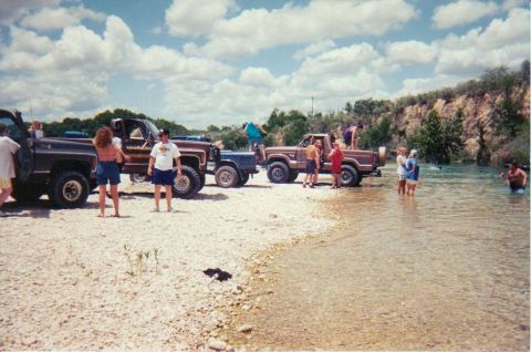 1989 Ford Bronco - People and trucks gather by the water on a sunny day.