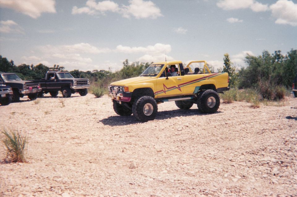 Yellow lifted pickup truck with red and yellow graphics, large off-road tires, and a roll bar
